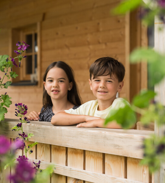 Bub und Mädchen stehen an der Terrasse und lachen in die Kamera.